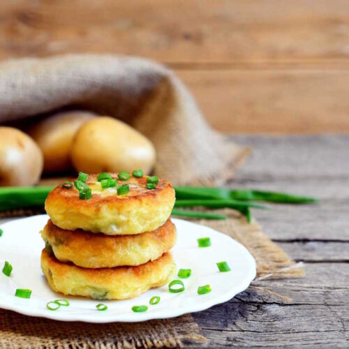 Golden crispy-coated vegan potato cakes, stacked on a plate.