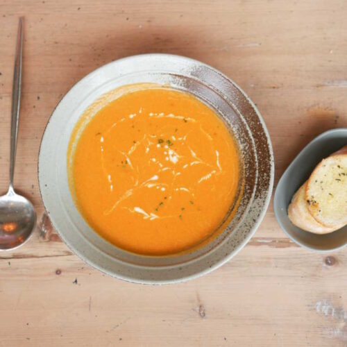 Colourful orange carrot and coriander soup with a side of warm bread.