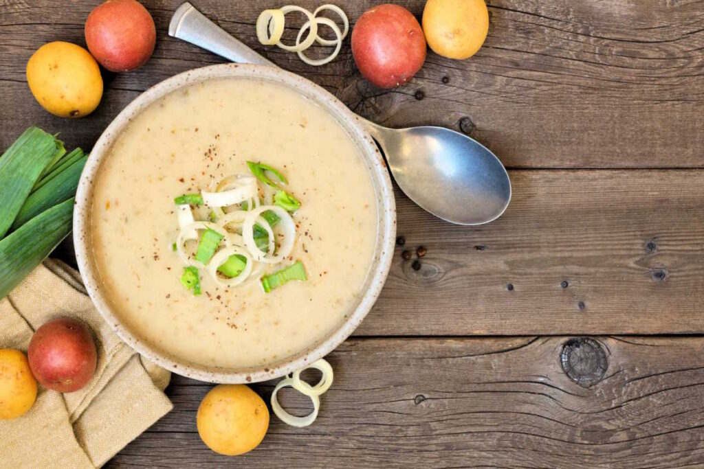 Vegan creamy leek and potato soup served with sliced leeks and seasoning to garnish.