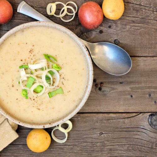 Vegan creamy leek and potato soup served with sliced leeks and seasoning to garnish.