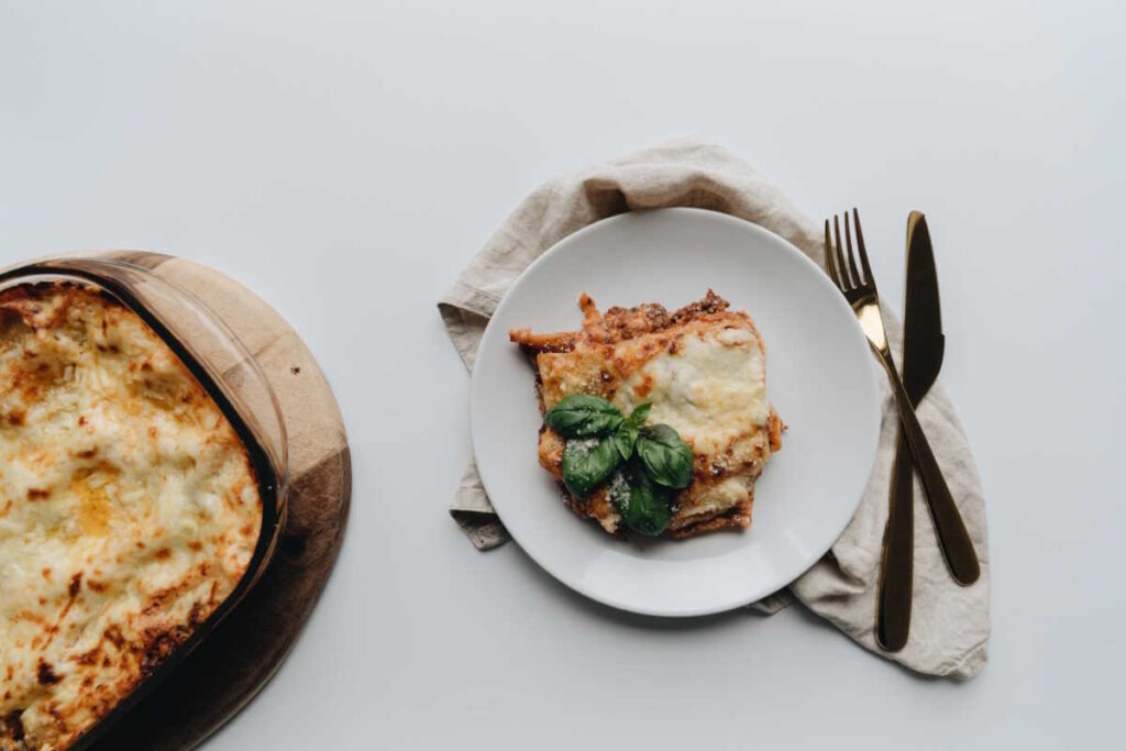 Vegan baked lasagne, with thick layers of red sauce, white sauce, pasta and dairy-free cheese. Served with a basil garnish.