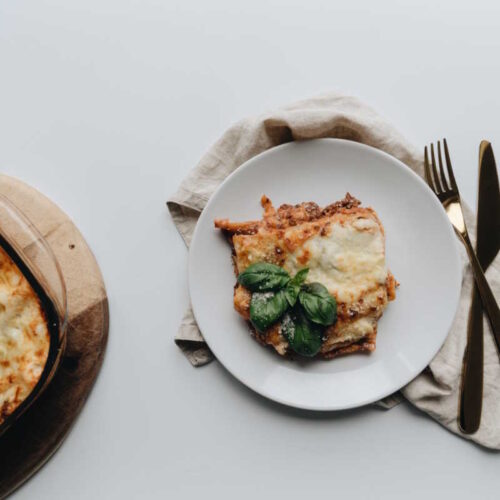 Vegan baked lasagne, with thick layers of red sauce, white sauce, pasta and dairy-free cheese. Served with a basil garnish.