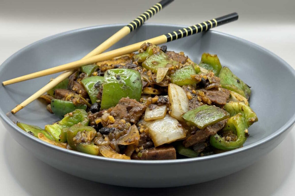 Bowl of Chinese-inspired vegan beef in black bean sauce, served hot and ready to eat with chopsticks.