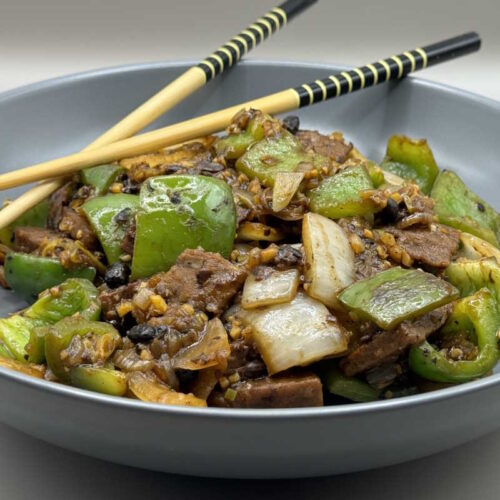 Bowl of Chinese-inspired vegan beef in black bean sauce, served hot and ready to eat with chopsticks.
