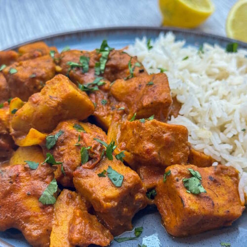 A plate of vegan chicken tikka masala garnished with lemon jusice and coriander, served with basmati rice.