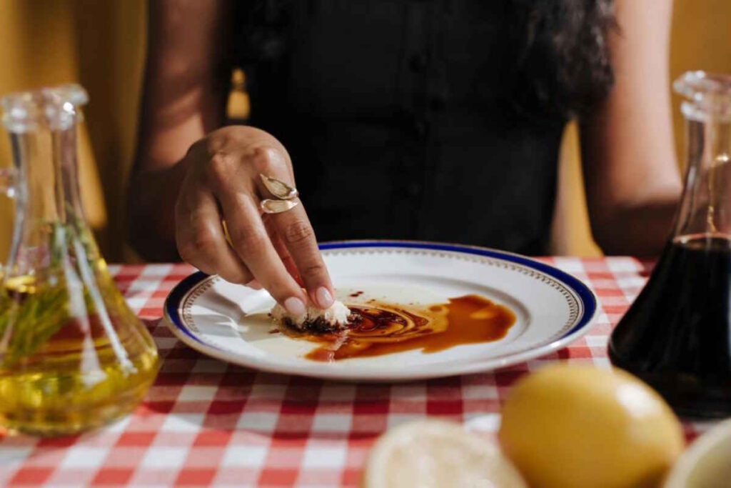 Woman soaking up traditional balsamic vinegar mixed with olive oil, into soft white bread.