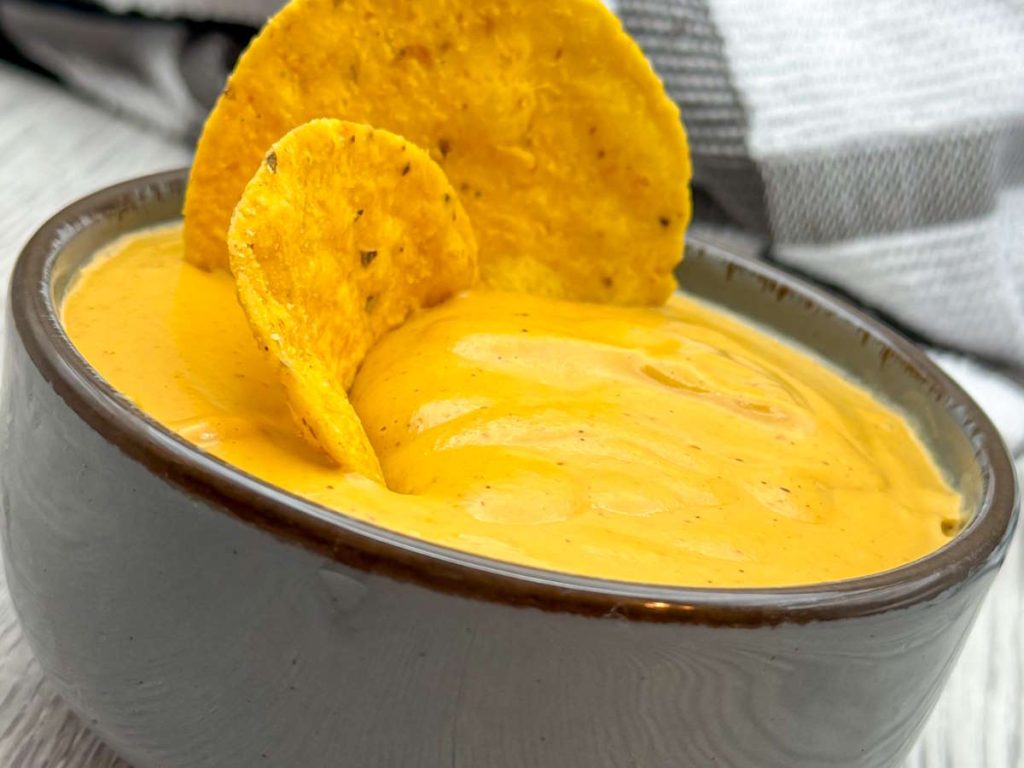 Plant-based queso-style dip made from cashews and soy milk with nutritional yeast served in a bowl with tortilla chips.