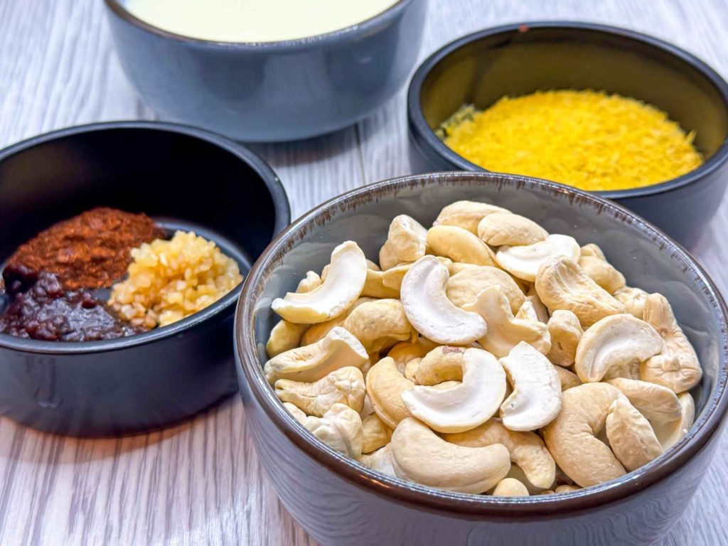 Plant-based queso-style dip ingredients, including raw cashews, minced garlic, spices, nutritional yeast, soy milk and spices.